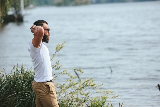 American Bearded Man sieht in einer blauen Jacke am Flussufer aus river