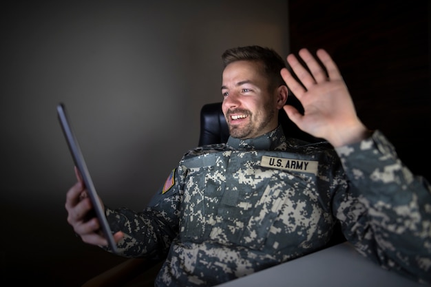 Kostenloses Foto amerikanischer dienstfreier soldat in militäruniform mit tablet-computer, der seiner familie winkt