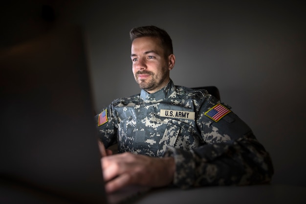 Amerikanischer Soldat in Militäruniform mit USA-Patch-Flaggen, die spät am Computer arbeiten