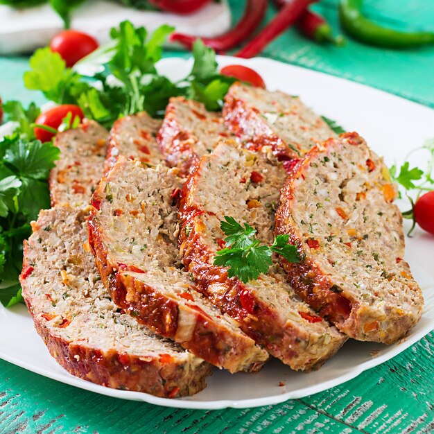 Amerikanisches Essen. Selbst gemachter Hackfleischhackbraten mit Ketschup und grünem Pfeffer. Fleischstück auf weißer Platte.