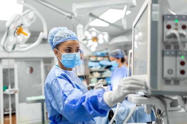 Anästhesist, der im Operationssaal arbeitet und Schutzausrüstung trägt, überprüft Monitore, während er den Patienten vor dem chirurgischen Eingriff im Krankenhaus sediert