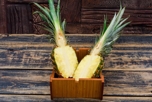 Ananas halbiert in einer Holzplatte auf alten Holz- und dunklen Steinfliesen, Seitenansicht.