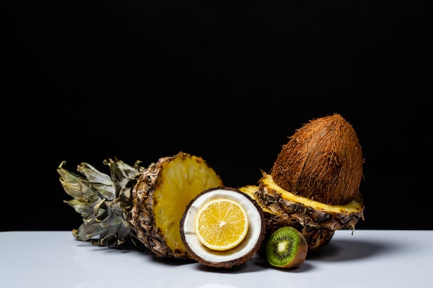 Ananas-Kokos-Orange und Kiwi halbiert auf einem Tisch auf einem schwarzen