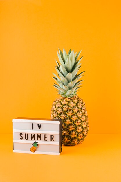 Ananas nahe dem Leuchtkasten mit Liebessommer des Wortes I gegen gelben Hintergrund