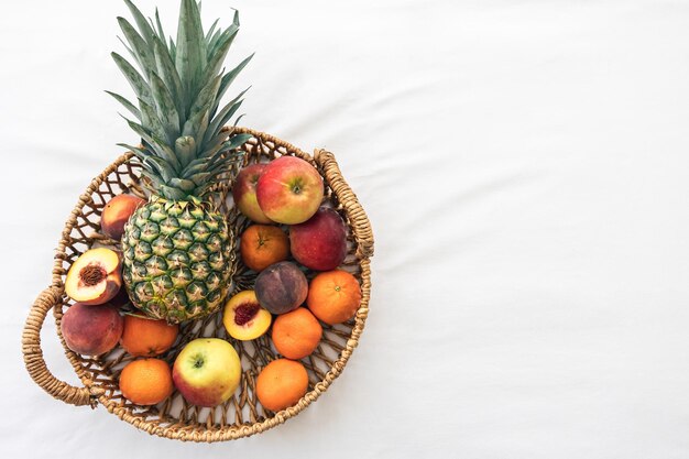 Ananas und andere exotische Früchte in einem Korb auf einer Draufsicht des weißen Hintergrundes