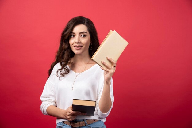 Kostenloses Foto anbietendes buch der brunettefrau auf rotem hintergrund. foto in hoher qualität