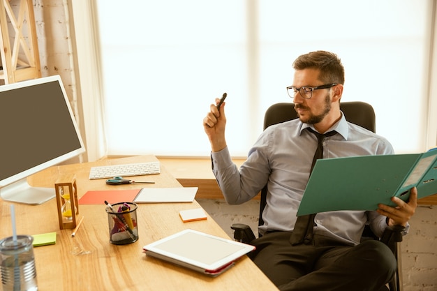 Angebote. Ein junger Geschäftsmann, der im Büro arbeitet und einen neuen Arbeitsplatz bekommt. Junger männlicher Büroangestellter beim Verwalten nach der Beförderung