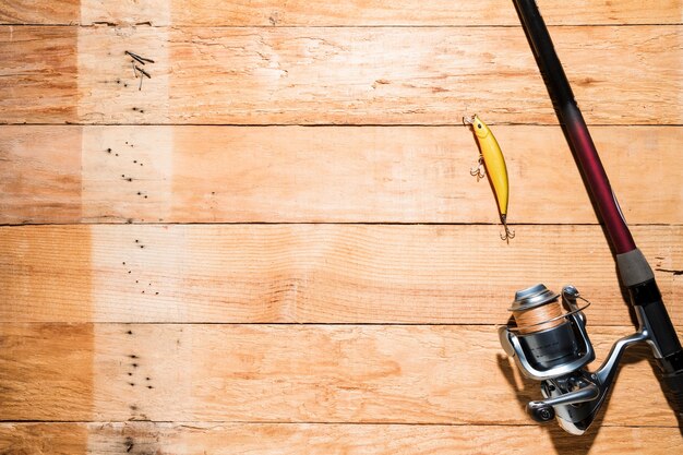 Angelrute mit gelbem Fischereiköder auf hölzerner Planke