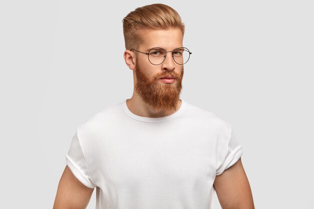 Angenehm aussehender ernsthafter Mann steht im Profil, hat selbstbewussten Ausdruck, trägt lässiges weißes T-Shirt