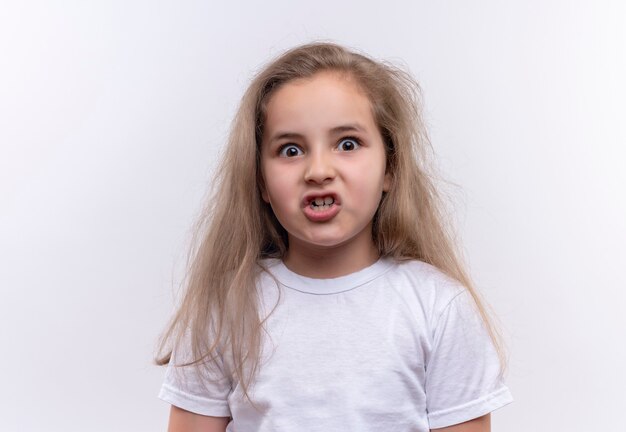 Angry kleines Schulmädchen, das weißes T-Shirt auf isolierter weißer Wand trägt