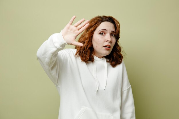 Angst, Hand in die Kamera zu halten junge Frau mit weißem Pullover isoliert auf grünem Hintergrund