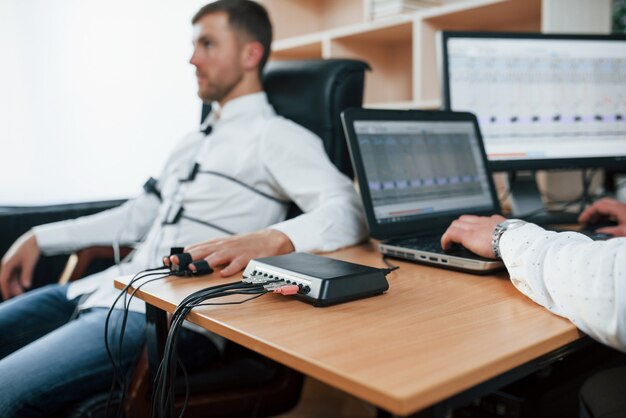 Angst zeigt, dass Sie nicht so ehrlich sind. Verdächtiger Mann übergibt Lügendetektor im Büro. Fragen stellen. Polygraphentest