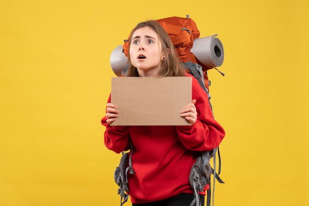 Kostenloses Foto anhalterin der vorderansicht mit rucksack, der leeren karton hält, der oben schaut