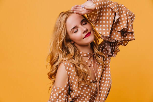 Anmutige junge Frau in der braunen Bluse, die Fotoshooting genießt. Nettes langhaariges Mädchen, das mit geschlossenen Augen aufwirft.