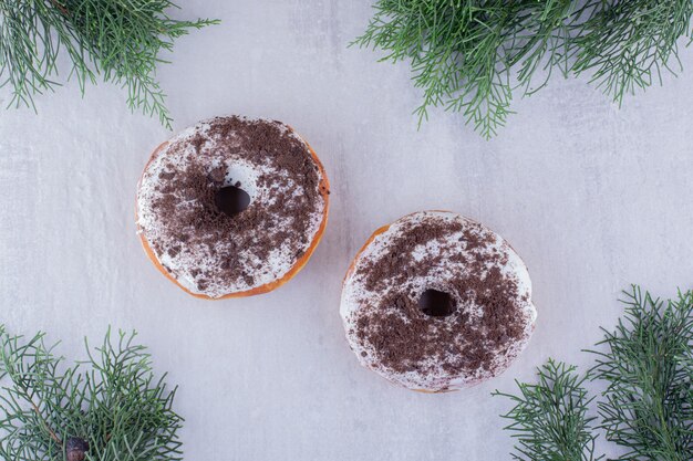 Anordnung von Donuts unter Zypressenblättern auf weißem Hintergrund.