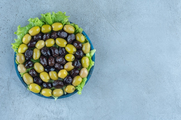 Kostenloses Foto anordnung von oliven ohne grube auf einer mit salat bedeckten platte auf einem marmortisch.