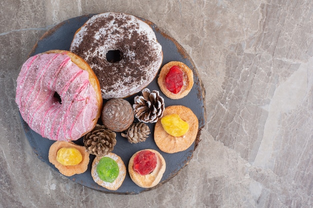 Anordnung von Tannenzapfen, Donuts und Keksen auf einem Brett auf Marmor.