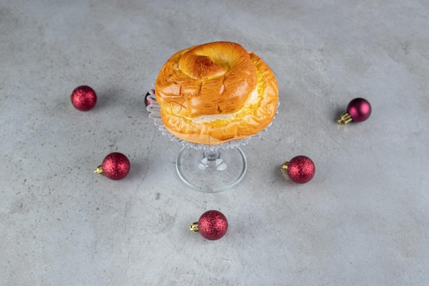 Kostenloses Foto anordnung von weihnachtsbaumspielzeugen um einen glassockel mit einem süßen brötchen auf marmortisch.