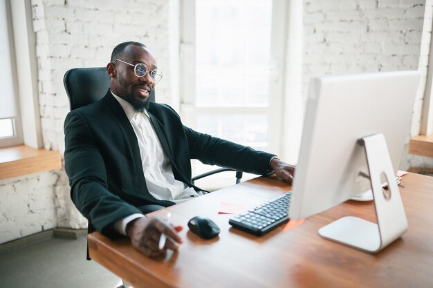 Anrufen, telefonieren. Afroamerikanischer Unternehmer, Geschäftsmann, der im Büro konzentriert arbeitet. Sieht ernst aus, beschäftigt, trägt einen klassischen Anzug. Konzept der Arbeit, Finanzen, Geschäft, Erfolg, Führung.