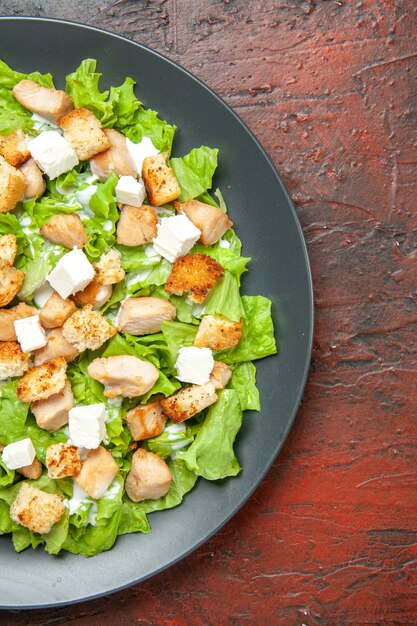 Ansicht der oberen Hälfte Caesar-Salat auf ovalem Teller auf dunkelrotem Hintergrund