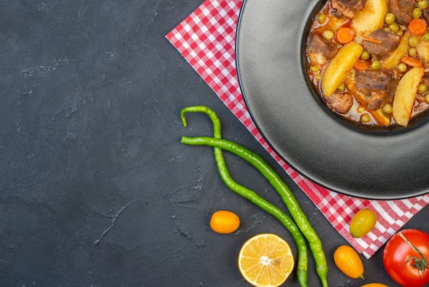 Ansicht der oberen Hälfte Fleischsuppe mit Garnitur auf rundem Teller frisches Gemüse auf schwarzem Tisch