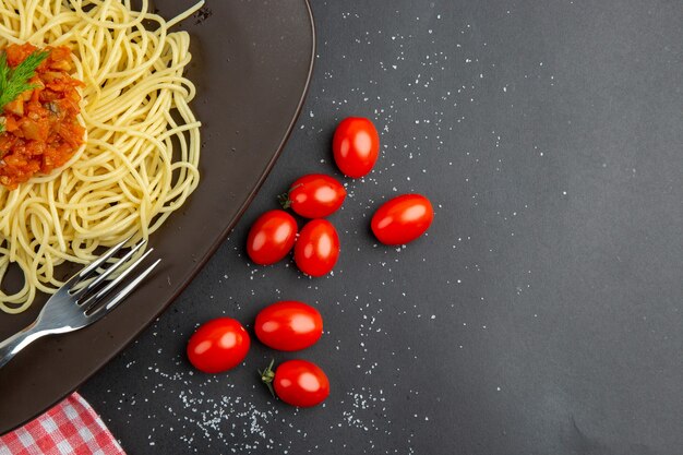 Ansicht der oberen Hälfte Spaghetti mit Soßengabel auf Tellerhandkirschtomaten auf schwarzem Tisch freier Platz