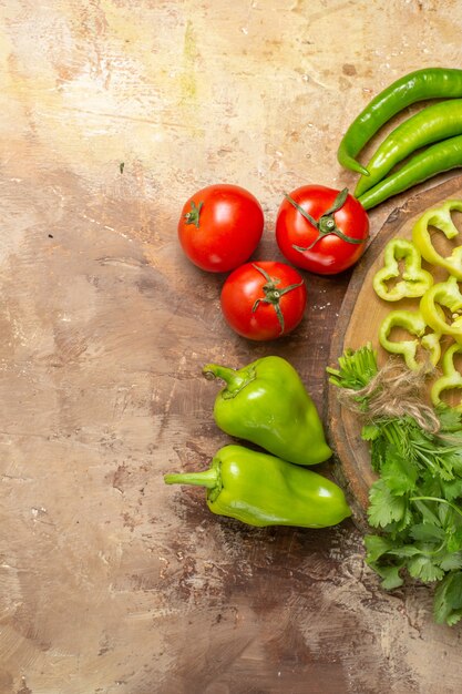 Ansicht der oberen Hälfte verschiedenes Gemüse, das auf runden Baumholzbretttomaten auf gelbem ockerfarbenem Hintergrund in Stücke geschnitten wird