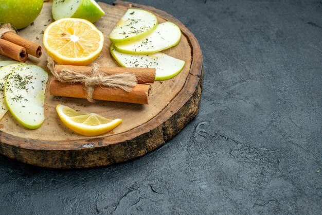 Ansicht der unteren Hälfte Apfelscheiben Zimt und Zitronenscheiben auf Holzbrett mit getrocknetem Minzpulver Apfel auf schwarzem Tisch