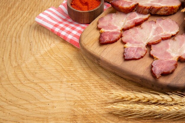 Ansicht der unteren Hälfte Becon-Scheiben auf Servierbrett rote Paprika in kleiner Schüssel Weizenspitze auf Holztisch wooden