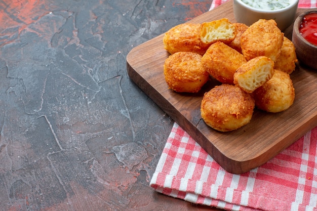 Ansicht der unteren Hälfte Chicken Nuggets auf Holzbrett mit Soßen rot-weiß kariertem Küchentuch auf dunklem Tisch