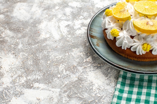 Ansicht der unteren Hälfte Kuchen mit weißer Gebäckcreme und Zitronenscheiben auf rundem Teller auf grün-weiß kariertem Tisch