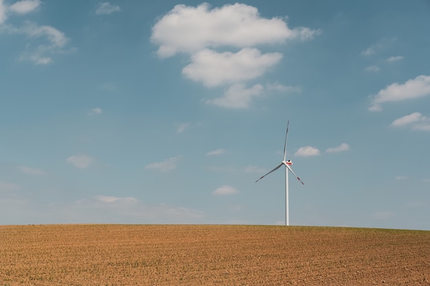 Ansicht der Windkraftanlage und der braunen Farm unter dem blauen Himmel und den weißen Wolken