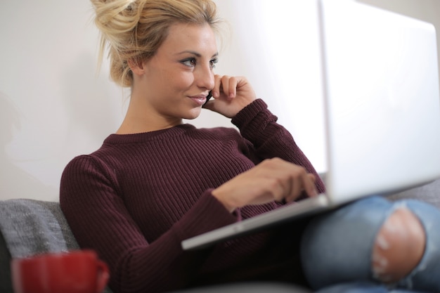 Ansicht einer schönen kaukasischen Frau, die auf der Couch sitzt, während sie am Laptop arbeitet und spricht