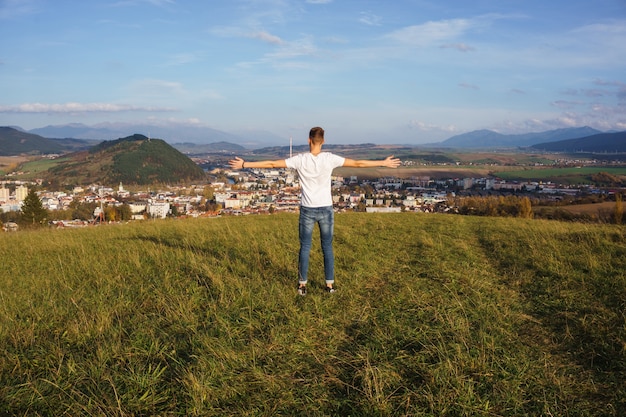 Ansicht eines Mannes, der mit offenen Armen auf einem Hügel steht, während er stolz seine Heimatstadt betrachtet