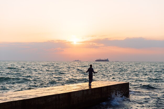 Ansicht in voller Länge des jungen Sportlers, der mit Springseil, auf Pier, nahe dem Meer springt.