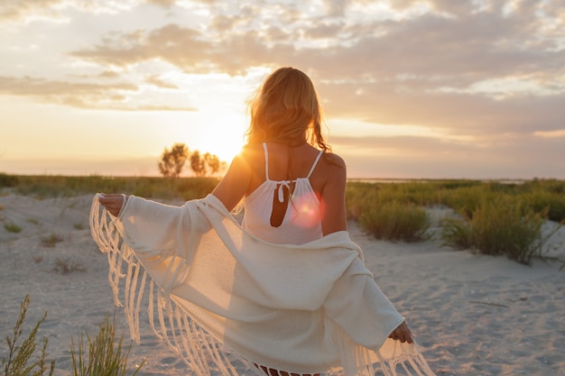 Ansicht von der Rückseite der anmutigen Ingwerfrau, die erstaunlichen Sonnenuntergang am Strand genießt.