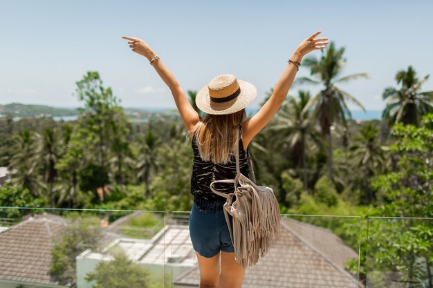 Ansicht von der Rückseite der reisenden Frau im Strohhut, die erstaunliche tropische Landschaft genießt