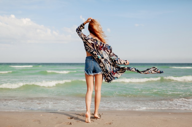 Ansicht von der Rückseite der sorglosen anmutigen Frau mit erstaunlichen Ingwerhaaren, die entlang des Strandes laufen