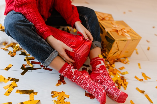 Ansicht von oben auf Frau in den roten Socken, die zu Weihnachten zu Hause auf goldenen Konfetti sitzen, die Ausstellungsstücke und Geschenkboxen auspacken
