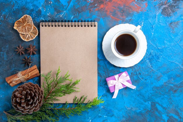 Ansicht von oben ein Notizbuch Kiefer Zweige Pinecone Sternanis eine Tasse Tee auf blauem Hintergrund