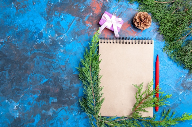 Ansicht von oben ein Notizbuch Pine Tree Branches Pinecone Rotstift auf blauem Hintergrund mit freiem Platz