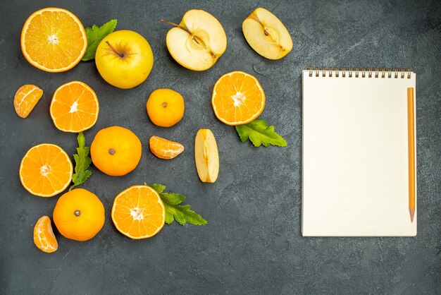 Ansicht von oben geschnittene Äpfel und Orangen ein Notizbuch auf dunklem Hintergrund
