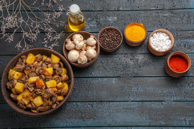 Ansicht von oben Schüssel mit Essen Holzschüssel mit Pilzen und Kartoffeln neben weißen Pilzen Öl bunte Gewürze und Zweige
