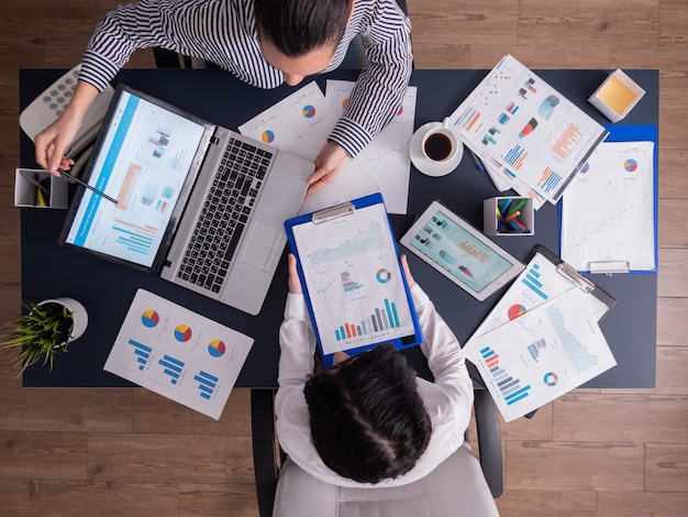 Ansicht von obenDraufsicht des Managers und des Mitarbeiters, der Teamarbeit im Geschäftsbüro macht, mit Blick auf Diagramme auf dem Laptop-Display