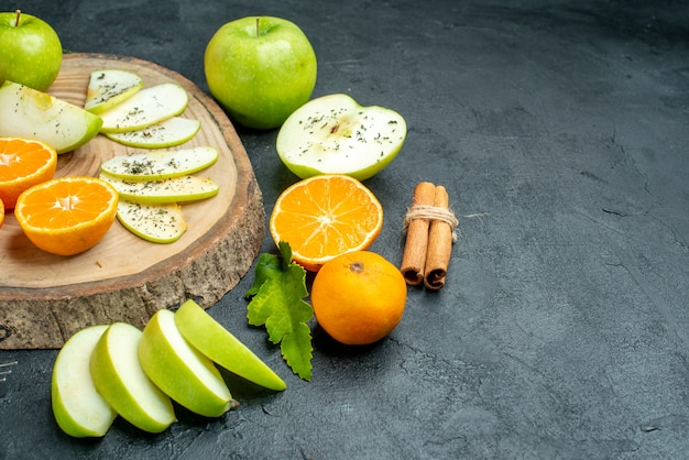 Ansicht von unten Apfel- und Mandarinenscheiben auf Holzbrett-Zimtstangen mit Seil auf schwarzem Tischkopierplatz gebunden