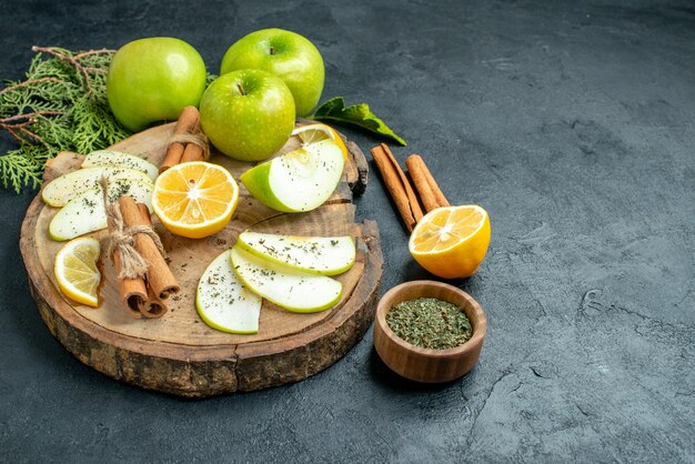 Ansicht von unten Apfelscheiben Zimtstangen und Zitronenscheiben Apfel auf Holzbrett geschnitten Zitronenzimt getrocknete Minze in kleiner Schüssel auf schwarzem Tisch mit Kopierraum