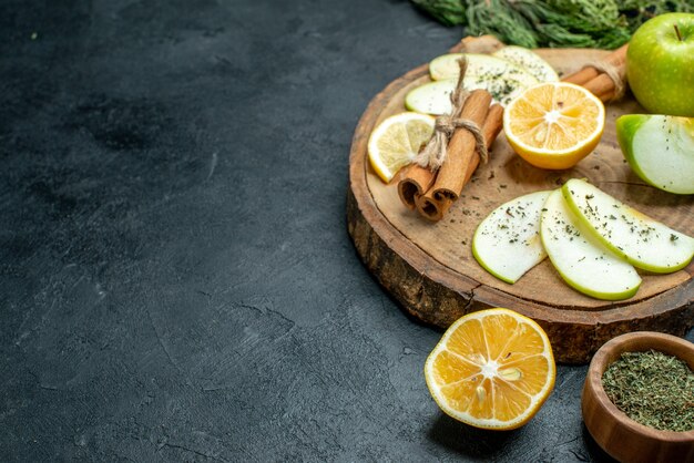 Ansicht von unten Apfelscheiben Zimtstangen und Zitronenscheiben Apfel auf Holzbrett Kiefernzweigen eine Gabel und ein Messer geschnittene zitronengetrocknete Minze auf schwarzem Tisch mit freiem Platz