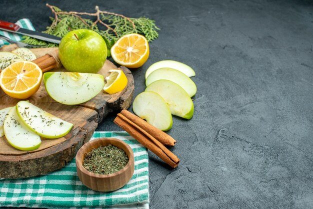 Ansicht von unten Apfelscheiben Zimtstangen und Zitronenscheiben Apfel auf Holzbrett Kiefernzweigen getrocknete Minzschale auf grüner Serviette auf schwarzem Tischfreiraum