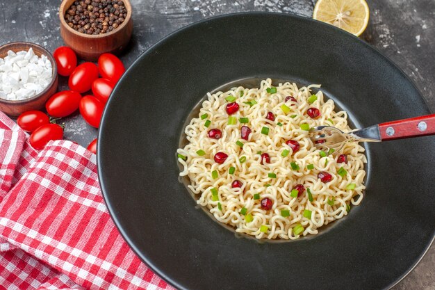 Ansicht von unten asiatische Ramen-Nudeln-Gabel auf schwarzem Teller geschnittene Zitronen-Kirschtomaten Meersalz schwarzer Pfeffer in kleinen Schüsseln auf dunklem Tisch