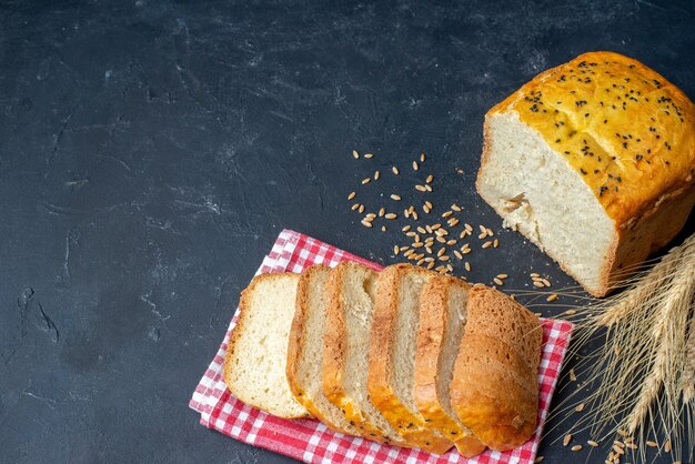 Ansicht von unten Brotscheiben auf rot-weiß karierten Küchentuch Weizenspitzen und Körnern auf dunklem Tisch freien Raum